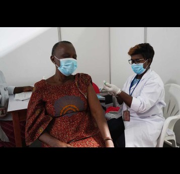 Health worker administering COVID-19 vaccine, both the patient and health worker are wearing a face mask. – Gavi/2021