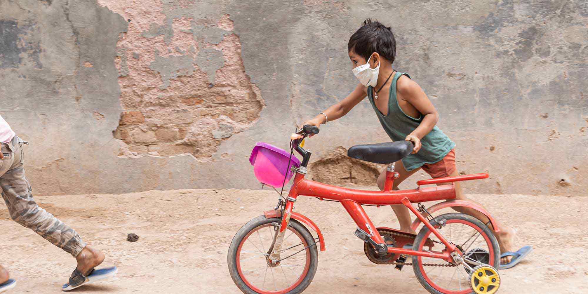 A young boy wearing a mask pushing his bicycle on a street in Rajasthan, India. Credit: Benedikt V. Loebell.