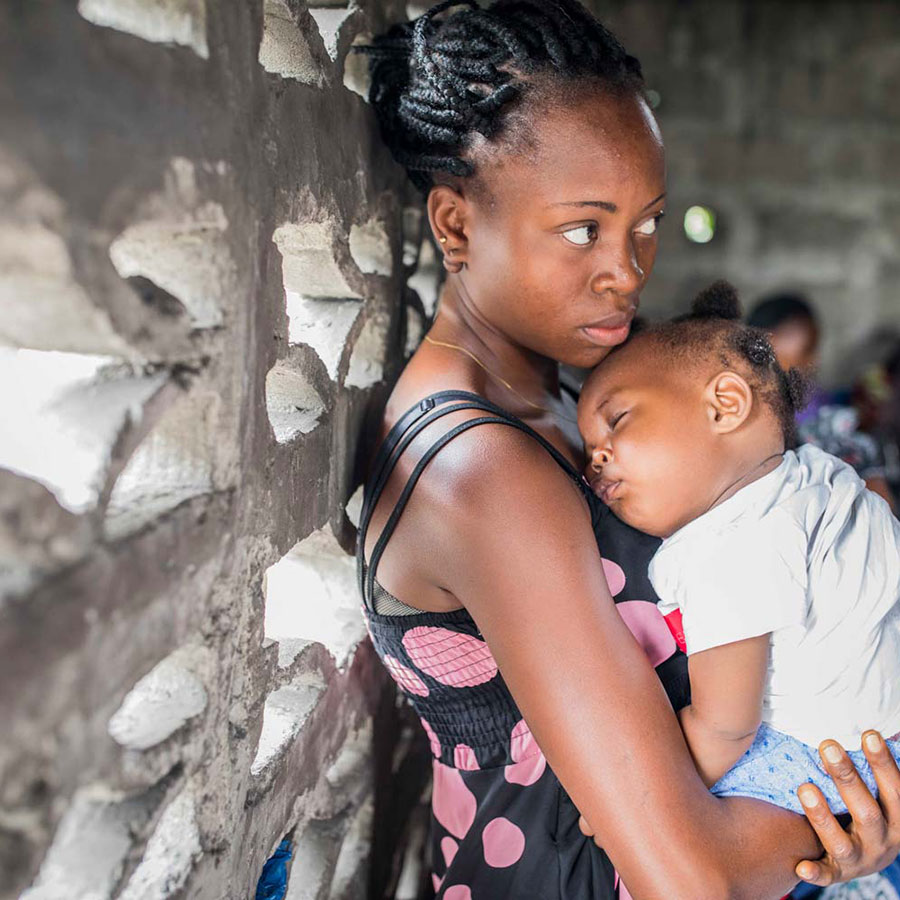 Mom leaning against the wall, holding baby - Photo credit: Gavi/2018/Thomas Nicolon