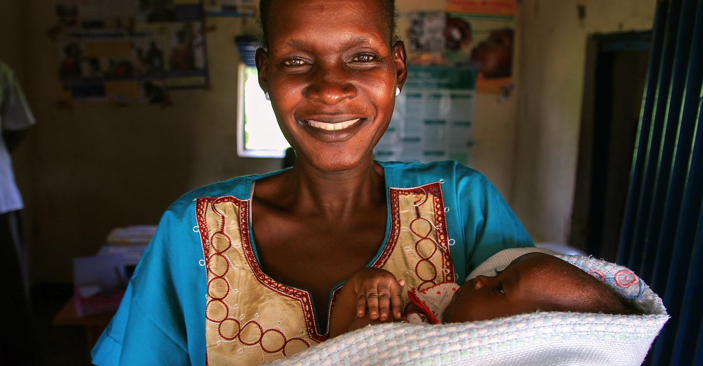 A woman smiles into the camera holding her baby during the pentavalent vaccine introduction in South Sudan.