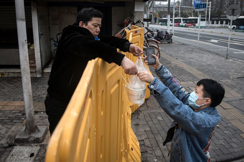 Image from Nature article – A man wearing a mask sells breakfast to nurses behind a makeshift barricade wall in Wuhan, China. Social distancing has been used to halt the transmission of the coronavirus in China. Credit: Getty Image from Nature article – A man wearing a mask sells breakfast to nurses behind a makeshift barricade wall in Wuhan, China. Social distancing has been used to halt the transmission of the coronavirus in China. Credit: Getty
