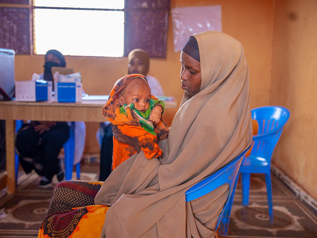 Muslima Ahmed holds her child as she waits for him to receive a dose of vaccine at the outreach vaccination facility in Somalia. Gavi/2024/Mohamed Abdihakim Ali