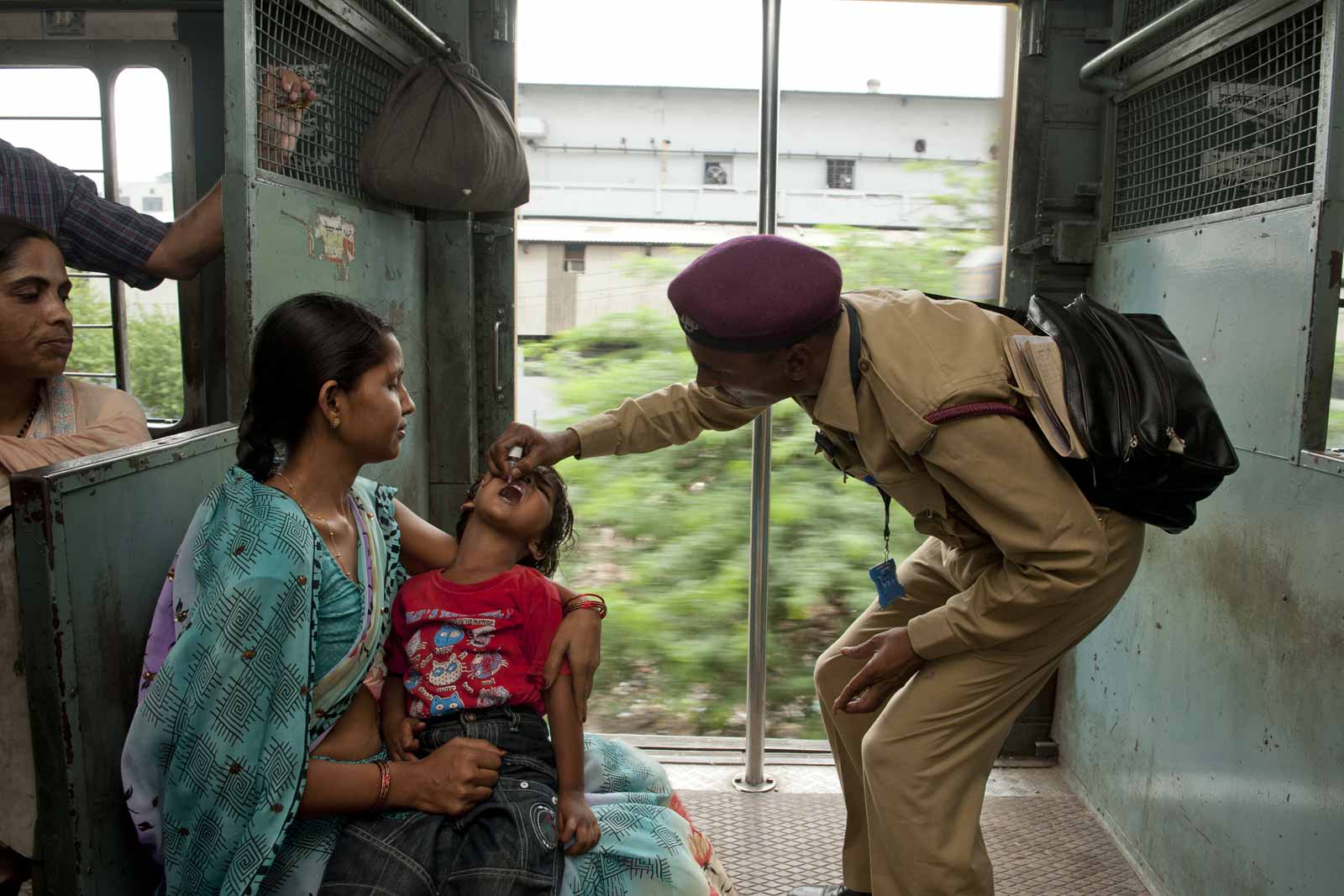   Archana, résidente de Dehradun dans l’État d’Uttarakhand regarde Ganga Das vacciner son fils Aush, âgé de quatre ans, contre la polio. La vaccination a lieu dans un train local à destination de Ghaziabad dans la banlieue de Delhi. Ces activités sont menées par des hommes uniquement. Lors de cette vaccination supplémentaire menée à l’échelle nationale, les femmes agents de santé administrent elles les vaccins en se rendant de maison en maison.