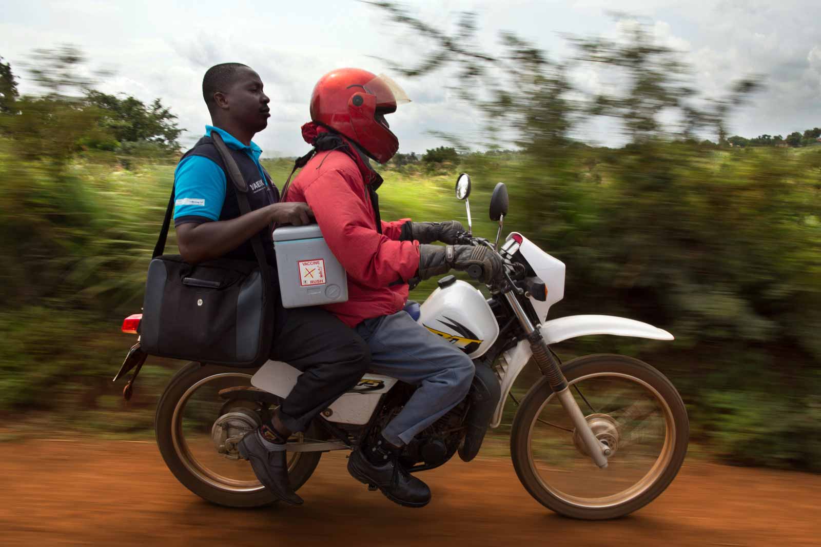 Data clerk Oscar Kai (blue shirt), carrying his laptop and a cooler of vaccines, heads to an outreach clinic by motorbike. Today he will gather data for a key research project - sponsored by GAVI - whose objective is to assess the impact of PCV on illness and deaths in the Kilifi district.