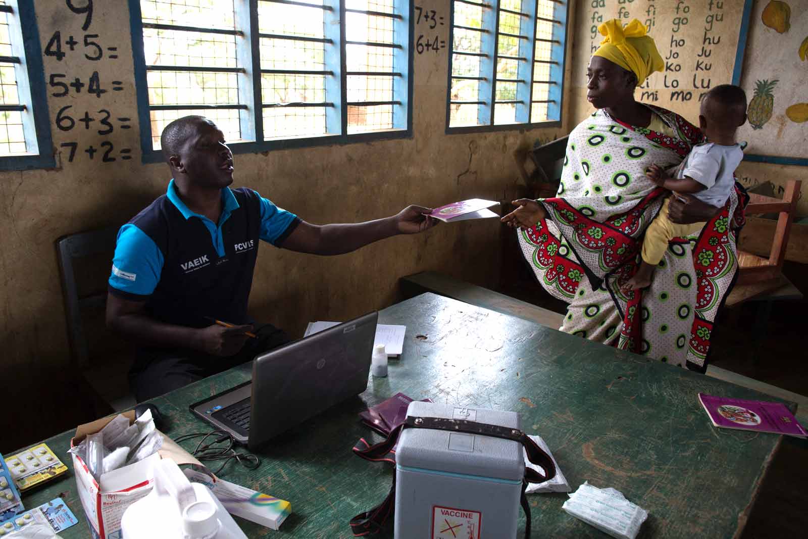  Oscar Kai hands a mother her child's medical record book. Kai has been entering patient information into his computer about the PCV and other vaccines children received today. All of that information is then uploaded to portable hard drives that are returned weekly to the study headquarters, where the database is updated.