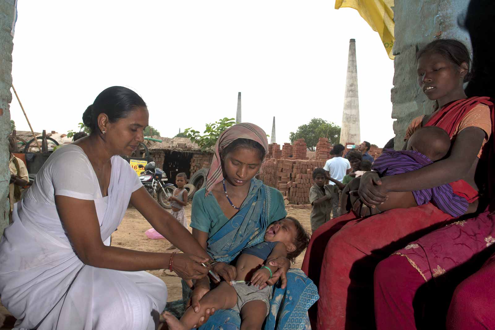  Auxiliary Nurse Midwife Shail Kumari administers a vaccine to Krishna Kumar with his mother Savita Devi, during a weekly visit to the Hunk brick kiln. With workers at the kiln working from 5-10am and 3.30-7pm, the clinics are held late morning to ensure no one is missed.Besides offering measles, polio, DTP, BCG and hepB vaccines for infants and children, pregnant woman can get TT shots and nutritional supplements.