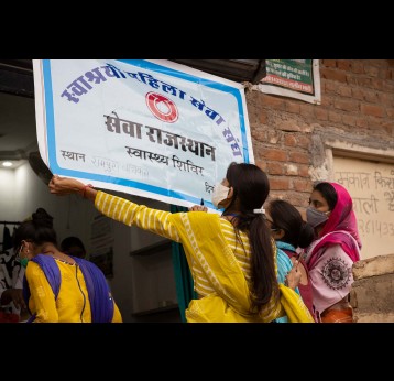 Ladies from the SEWA.org initiative are hanging up a sign for locals to know that they can get vaccinated against COVID-19 at this station, Bikaner, Rajasthan, India – Credit: Benedikt V. Loebell