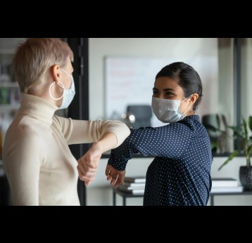 Colleagues respecting safety measures, wearing protective face masks greeting bumping elbows.