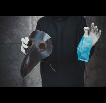 Man holds a mask of plague doctor and disposable medical mask.