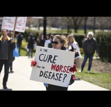 An activist with a sign comparing cure and disease during a rally to protest provincial and federal shut down to control the spread of COVID-19