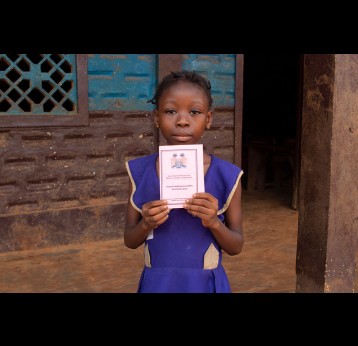 A girl at War Wounded Primary School in Grafton, Freetown, holds up her vaccination card. Credit: Abdul Aziz Kamara