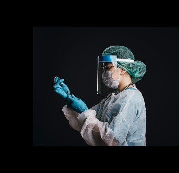 A female doctor wearing a Protection suit with a stethoscope against COVID-19 holding syringe and vaccine on black background