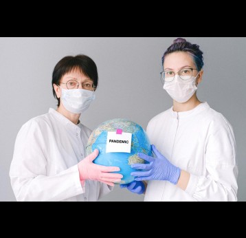 Women with lab coats, gloves and face masks holding a globe. Credit: Anna Shvets on Pexels