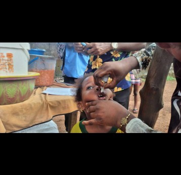 Un enfant reçoit une dose de vaccin contre la polio à côté de sa maman vendeuse de haricots à Dabompa, Conakry. Crédit : Alpha Abdoullaye Diallo