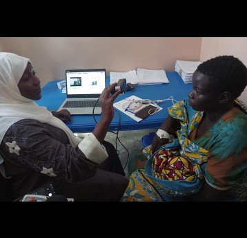 Rukia Hassan Ali a supervisor at Nagasaki University Institute of Tropical Medicine NUITM-KEMRI, taking pictures and details of Mishi Gulu and her infant for biometric vaccination in Kinango hospital. Credit: Diana Wanyonyi