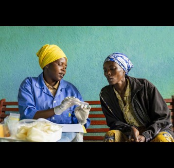 A community health worker speaks with a woman about available health services in Rwanda. Tens of thousands of CHWs deliver essential care, from malaria treatment to cervical cancer prevention. Credit: RBC