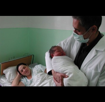 In a Uzbekistan hospital, a doctor holds a baby while the mother looks on from her hospital bed. Credit: Gavi/2013/Thomas Kelly