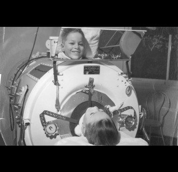 Boy in Emerson respirator (iron lung) in Herman Keifer Hospital, Detroit, Michigan, due to polio. Viewing photographer (Joe Clark) in machine's mirror. Ca. 1955. Credit: Otis Historical Archives National Museum of Health and Medicine