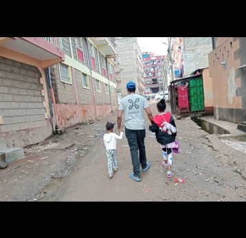 A father walking hand-in-hand with two young daughters down a muddy street in an urbanising Samburu town. Credit: Gitonga Njeru