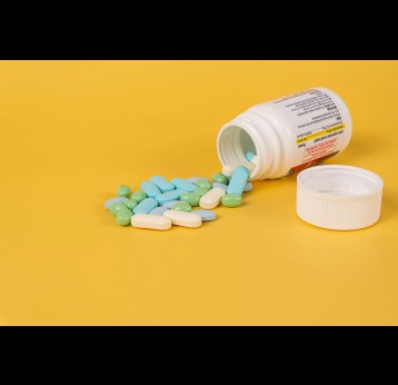 An assortment of pills spilling out of a medication bottle on a pastel orange background. Photo by Etactics Inc on Unsplash