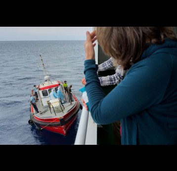 Passengers on the the hantavirus-stricken cruise ship MV Hondius watch epidemiologists board the boat in Praia, Cape Verde, on May 6, 2026. AP Photo/Uncredited