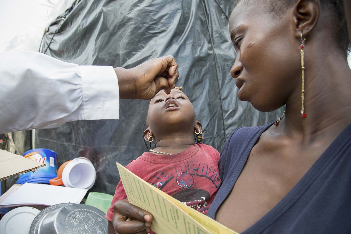 Nurses Sall Rougui Niang (left, out of shot) gives vitamin drops to Fatoumata (centre), a 20-month-old girl living in Nabisouikr – one of the city's slums. Credit: Gavi/2018/Simon Davis