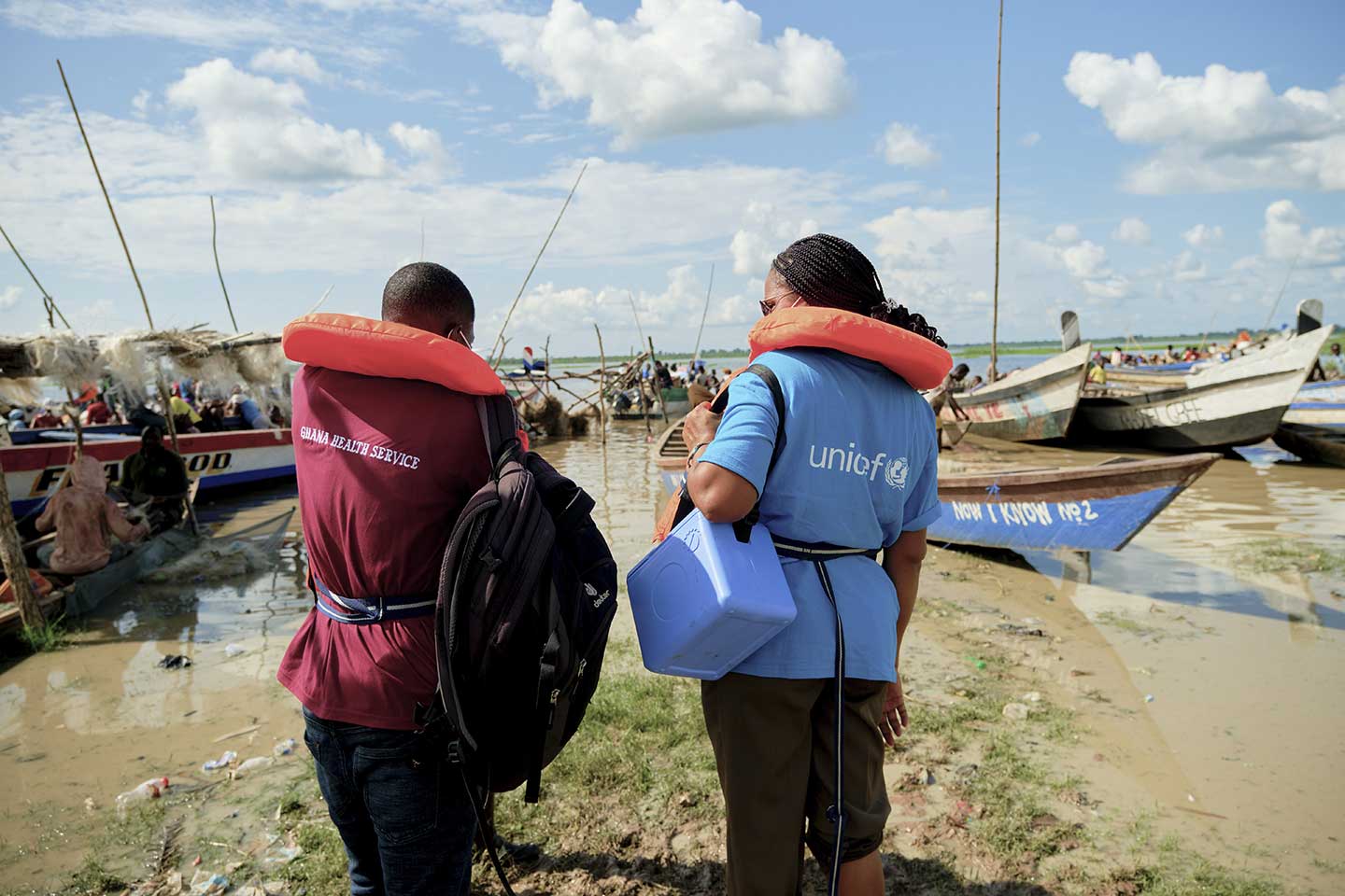 UNICEF Communication for Development Officer, Charity Nikoi waits on the bank of the Afram River with Health Officer, Francis Teye in Sempoa in the Eastern Region. The team were preparing to cross the river to reach children on the other side on 8 October 2020. ©UNICEF/ANNANKRA