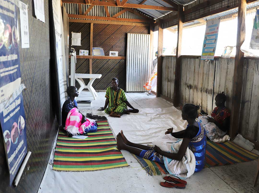 A group of women sit on mats in the clinic, waiting for their children to receive routine vaccines © IOM 2020 / Liatile Putsoa