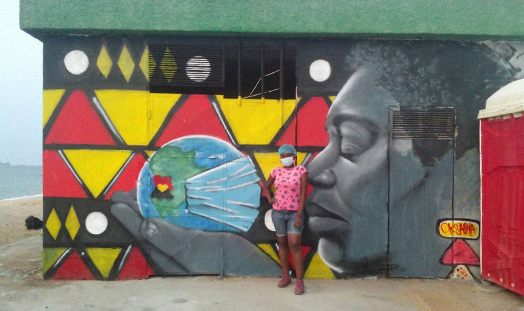 Oksanna Dias stands in front of her mural showing earth protected by a surgical mask.