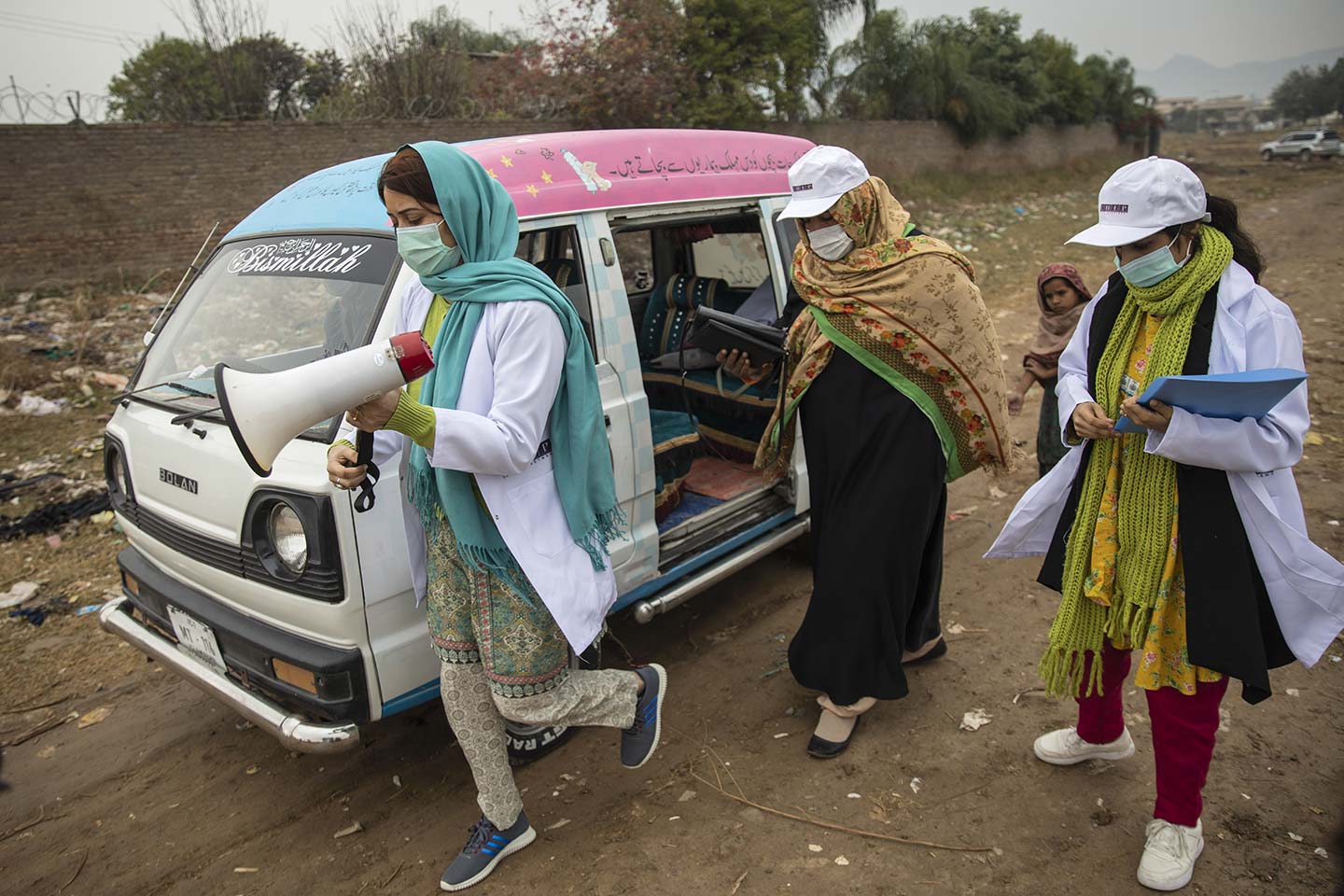 Sadaf Fareed (left) and her team walk towards the tented homes in slum making announcements.  Credit: Gavi/2020/Asad Zaidi