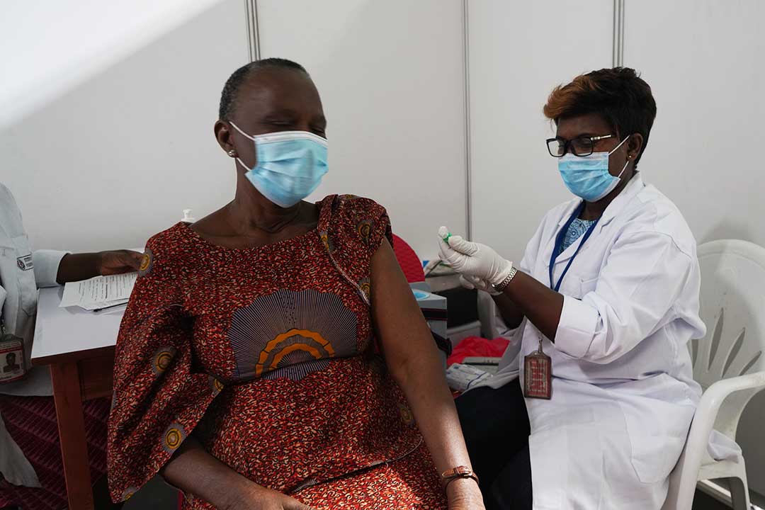Health worker administering COVID-19 vaccine, both the patient and health worker are wearing a face mask. – Gavi/2021