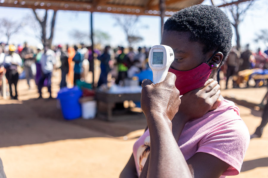 A young woman has her temperature checked as hundreds of residents wait to receive their first dose of COVID-19 vaccine at Ngozi Mine.