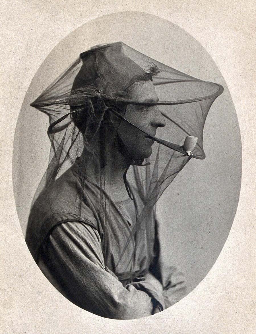 Mosquito headnet with cap and breathing pipe, modelled by a man in profile. Photograph, 1902/1918 (?).. Credit: Wellcome Collection. Public Domain Mark