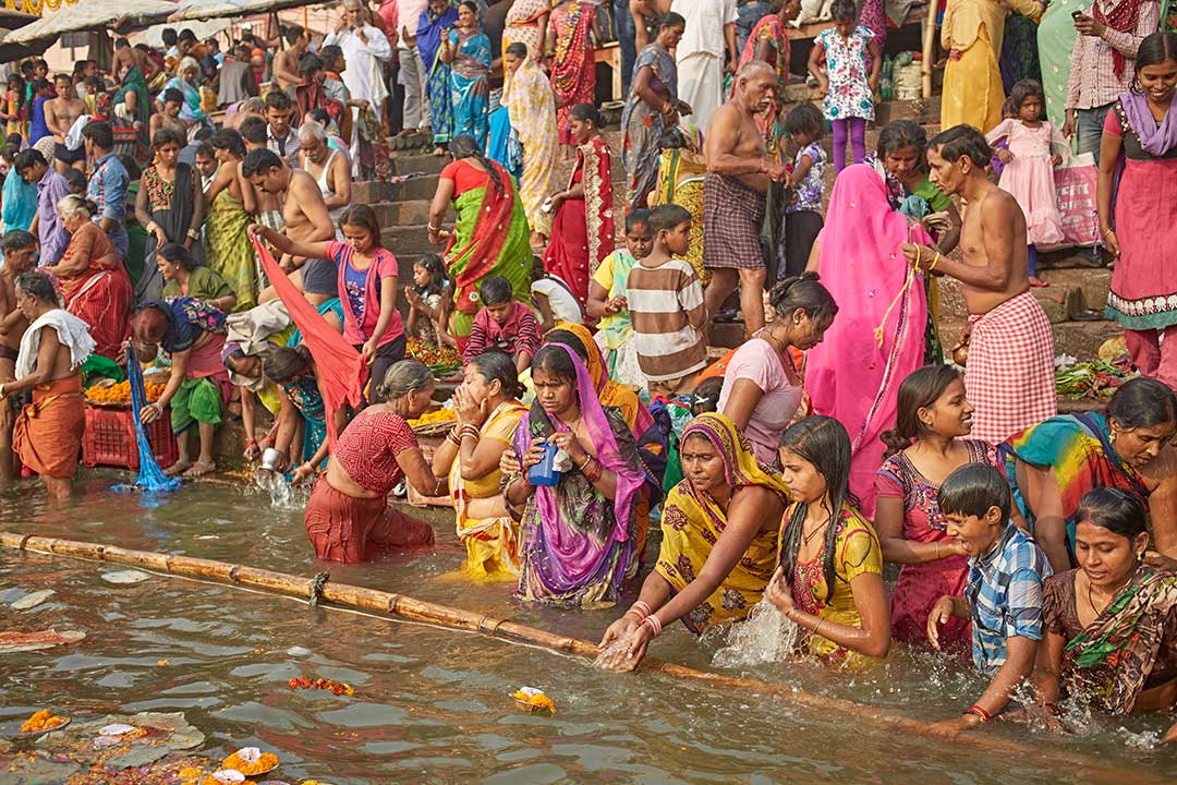 A crowd in a sacred ritual bath in a Ganges River ghat at dawn.