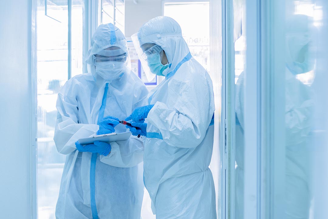 Two asian woman doctor in personal protective suit or PPE with mask writing on quarantine patient chart, holding test tube with blood sample for screening coronavirus.