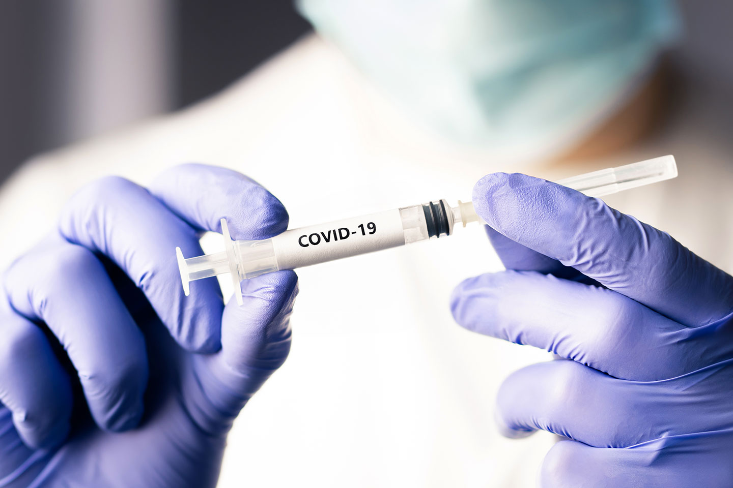 Doctor or nurse working in health care wearing a mask holding a COVID-19 syringe