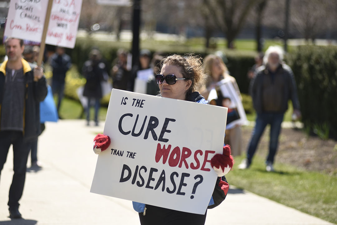 An activist with a sign comparing cure and disease during a rally to protest provincial and federal shut down to control the spread of COVID-19