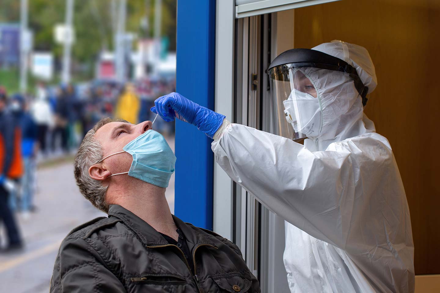Medical worker in protective gear collects a sample from man during pandemic of COVID-19.