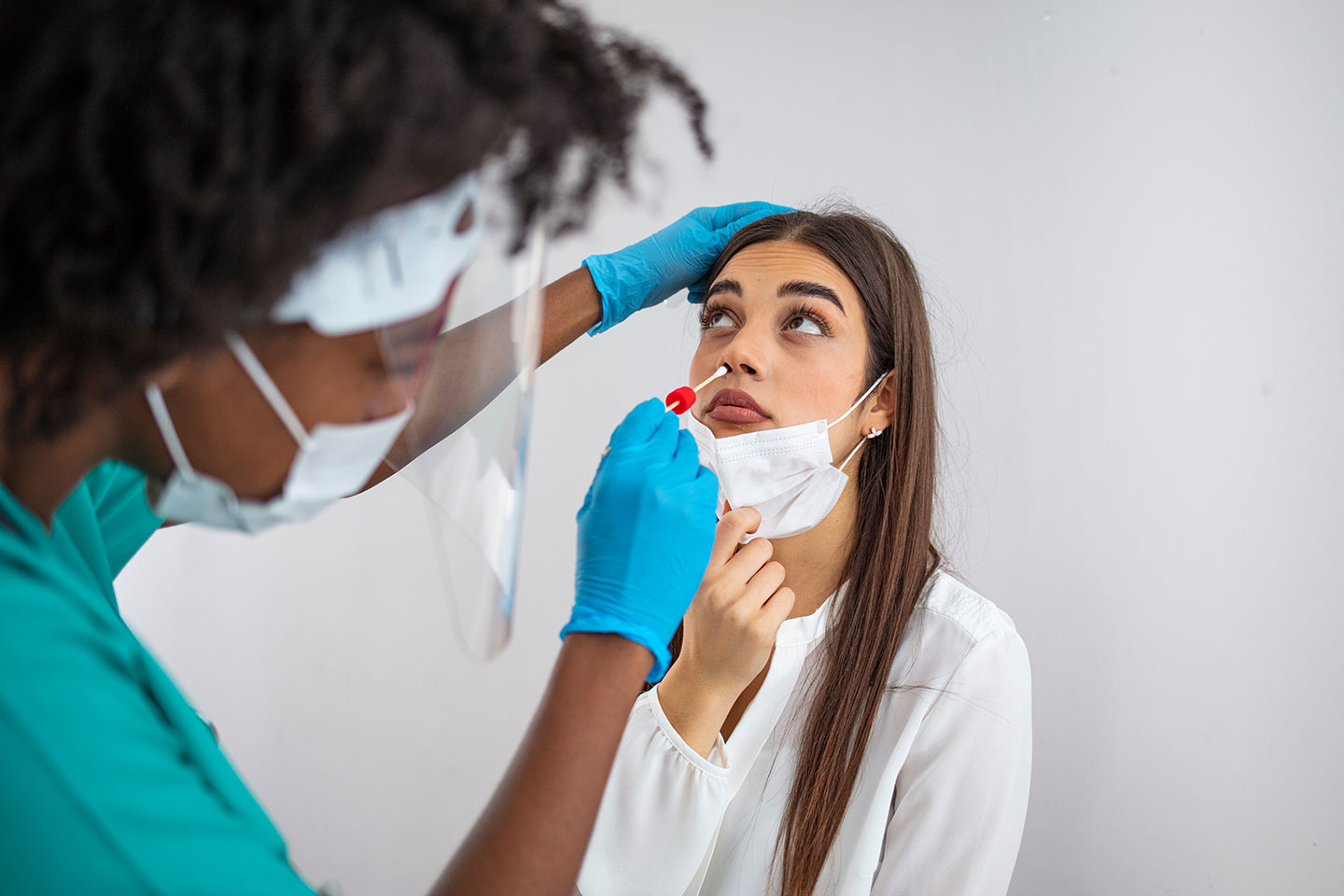Doctor in protective workwear taking nose swab test from young woman. Close-up of woman having PCR testing at the hospital.