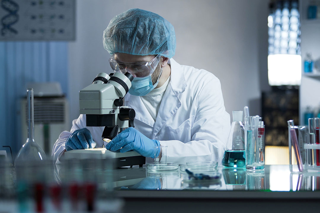 Scientist looking into a microscope with protective equipment on.