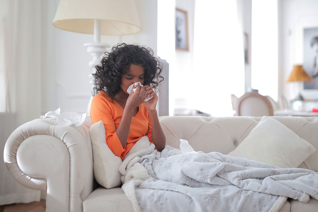 Woman wiping her nose with tissue laying on the couch. Photo by Andrea Piacquadio from Pexels
