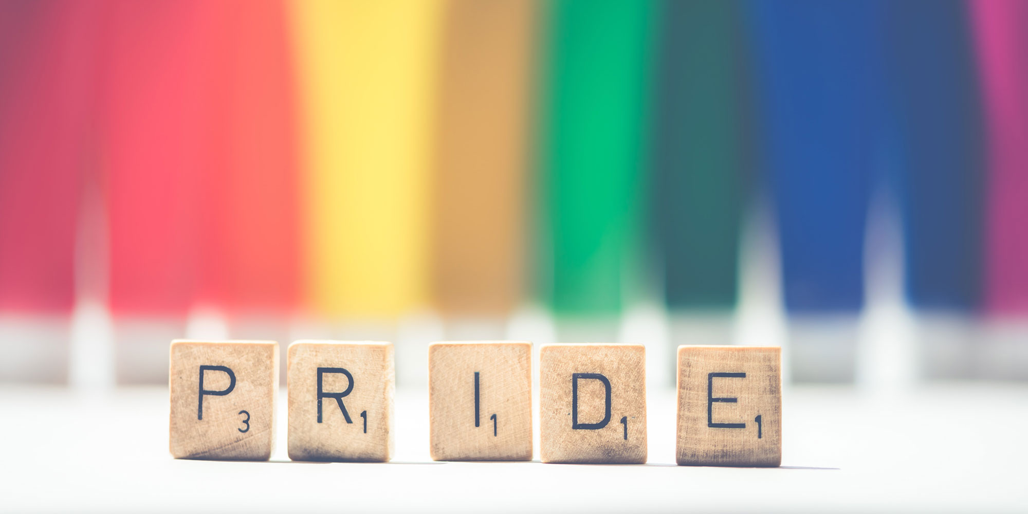 Selective focus photograph of Scrabble tiles spelling PRIDE against a rainbow backdrop. Photo by Ylanite Koppens from Pexels