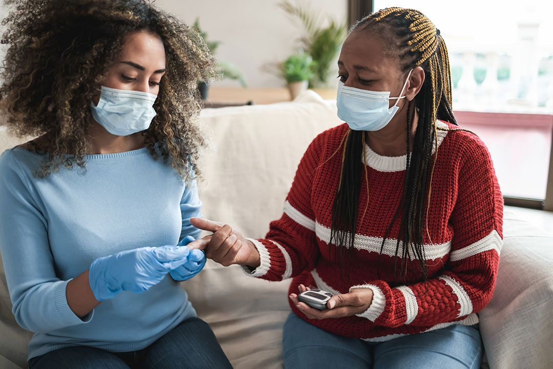 Young african nurse taking blood from senior patient for diabetes exam at home.