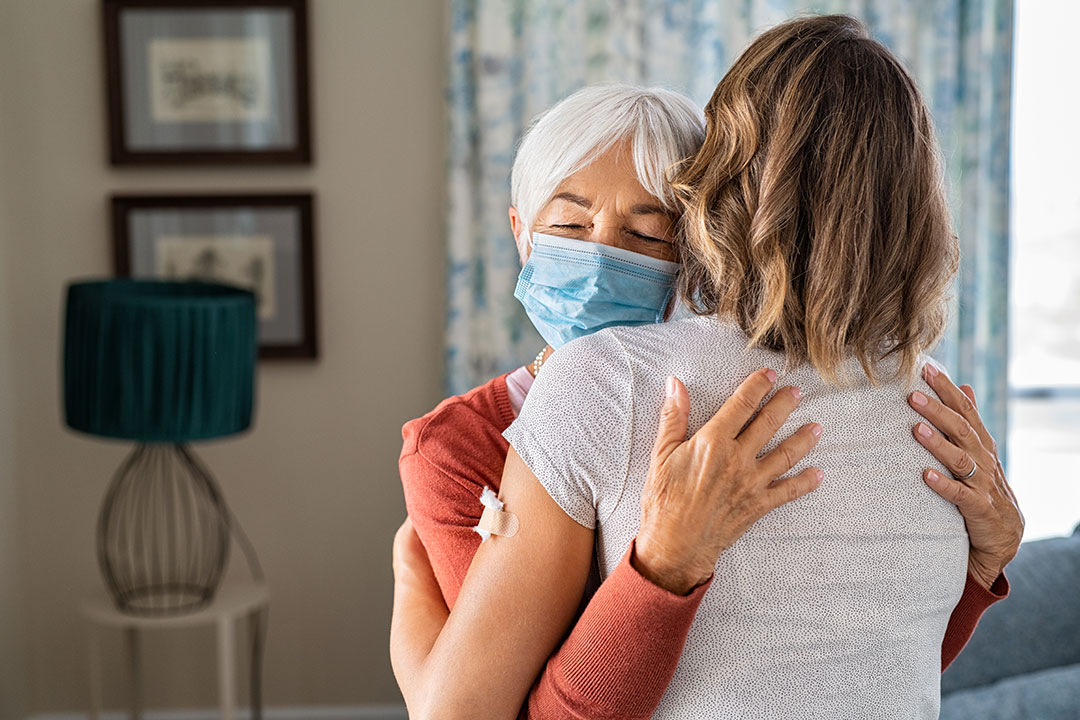 Senior woman wearing face mask hugging immunized daughter after covid-19 vaccination shot.