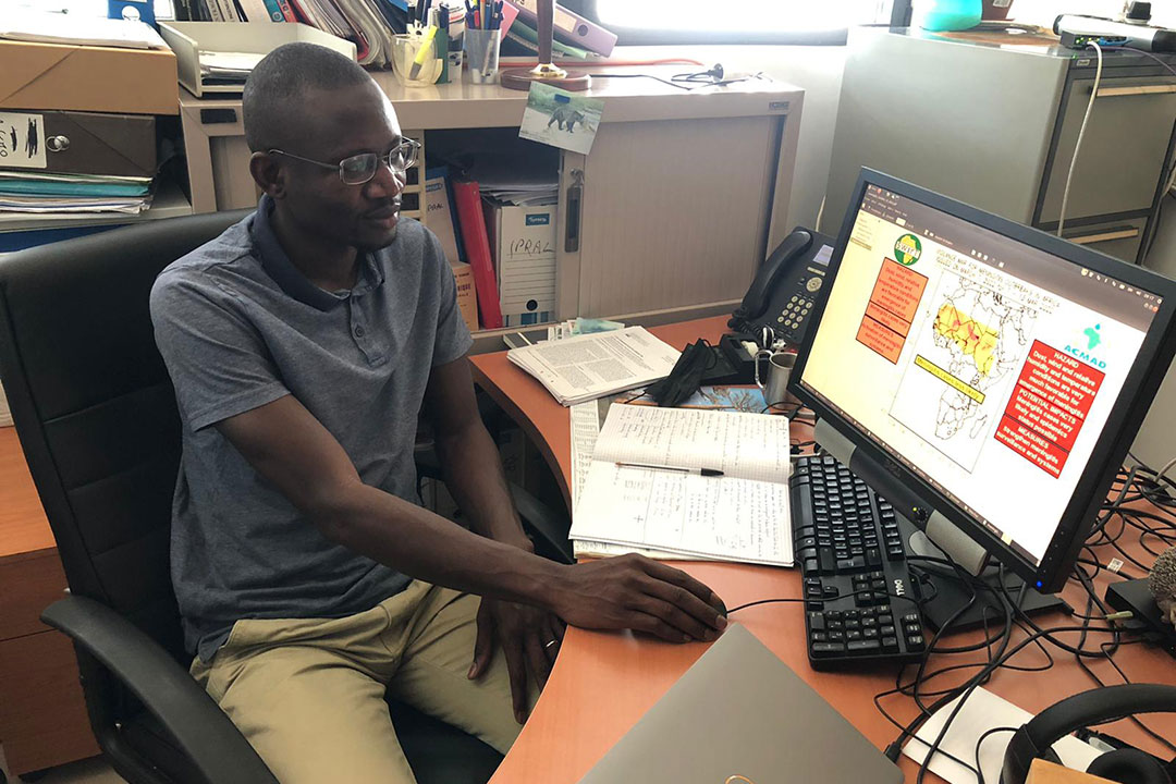 Dr Cheikh Dione at his desk, with a meningitis prediction report open on his computer.