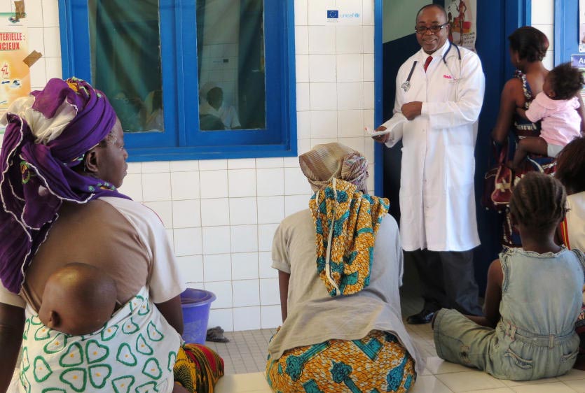Women with children on their backs listen to a physician at a health facility in Cote d'Ivoire. Copyright: Anouk Delafortrie/ECHO. (CC BY-ND 2.0).