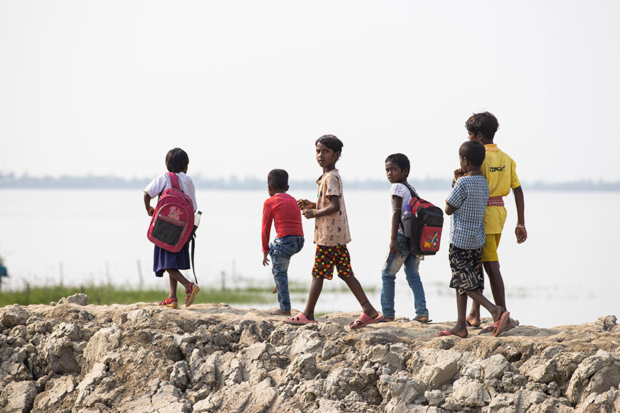 A group of schoolchildren walk on a dam in the Indian Sundarbans. Gavi/2022/Benedikt v.Loebell