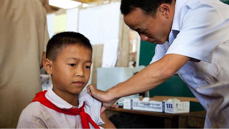 Savannakhet Regional Health Director, Dr Inpone Maniseng administers a measles vaccine jab to a young boy. Credit Nittana Ketkesone