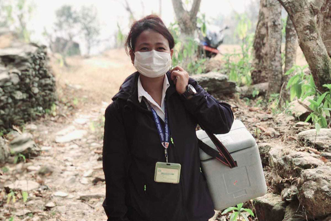 Kabita Chaudhari, senior health worker from Dhola Health Post in Jwalamukhi Rural Municipality, Dhading, on her way to the vaccination booth, carrying her ice-packed vaccine carrier. Credit : Chhatra Karki