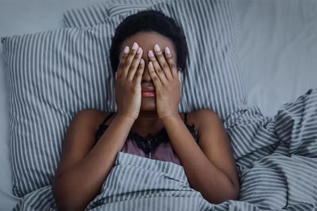 Woman in bed, covering her face in her hands. Credit: Prostock-studio/Shutterstock